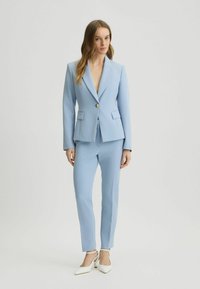 Costum personalizat de culoare albastru deschis, cu o jachetă structurată cu un singur nasture și pantaloni drepți. Textură netedă, cu detalii minime.