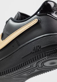 Gros plan d'une basket noire avec un swoosh Nike beige, montrant des coutures détaillées et la semelle texturée marquée "AIR."