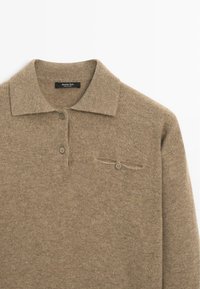 Polo marron en maille à manches longues avec col, trois boutons sur le devant et une petite poche boutonnée sur la poitrine gauche.