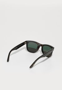 Ochelari de soare cu model tartău, cu lentile verzi, formă pătrată, finisaj lucios și accente metalice pe tâmple, având un logo subtil al brandului.