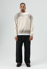 Oversized crèmekleurig sweatshirt met een verloopkleur, met "REBELLOON" in druppelende zilveren letters. Gecombineerd met losse zwarte spijkerbroek.