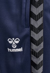 Marine trainingshort met een zwarte streep en een visgraatpatroon. Bevat een wit "hummel" logo aan de voorkant. Gladde textuur.