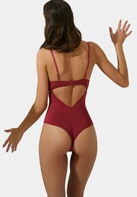 Maillot de bain une pièce rouge avec de fines bretelles, une découpe profonde dans le dos et un design de jambe haute. Texture lisse au style minimaliste.