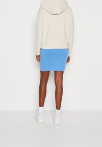 Sudadera con capucha beige combinada con una falda ajustada azul. La modelo lleva zapatillas blancas con calcetines de tobillo. Diseño sencillo y deportivo con texturas suaves.