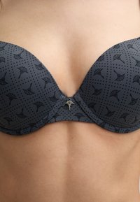 Gray molded bra with a patterned texture featuring floral designs and polka dots. Small metallic charm at the center front.