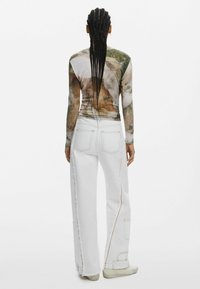 Langarmtop met aardse grafische print, gecombineerd met witte wijde jeans met stikdetails en een lichtgerafeld zoom.