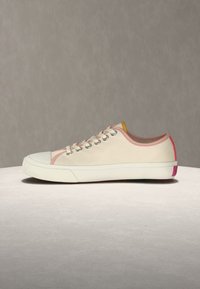 Μπεζ αθλητικό παπούτσι χαμηλού ύψους από καμβά με άσπρη λαστιχένια σόλα, ροζ περίγραμμα γύρω από το άνοιγμα, ασημί οπές για τα κορδόνια και ροζ λεπτομέρεια στην ετικέτα της φτέρνας.