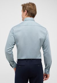 Patroonoverhemd van lichte blauwe stof, met een klein geometrisch ontwerp, lange mouwen en een spread collar, gedragen met donkere broeken.