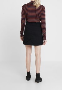 Černá džínová sukně ve tvaru A spárovaná s tmavým proužkovaným dlouhým rukávem, pohled zezadu. Textura je hladká s jemnými detaily.