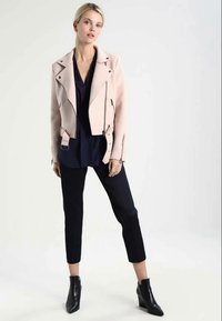 Ανοιχτό ροζ, κοντό μπουφάν μοτοσικλέτας με ασημένια κουμπώματα και φερμουάρ, φοριέται πάνω από ένα σκούρο μπλε μπλουζάκι και συνδυάζεται με μαύρους tapered παντελόνες και μποτάκια μέχρι τον αστράγαλο.