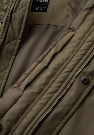 Olive green quilted jacket with a smooth inner lining, front zip closure, and button accents. Features multiple interior pockets.