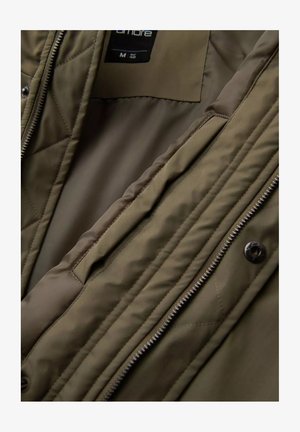 Olive green quilted jacket with a smooth inner lining, front zip closure, and button accents. Features multiple interior pockets.