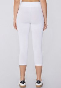 Witte leggings met een hoge tailleband, een cropped lengte en een gladde textuur. Gekocht met witte sneakers met zwarte accenten.