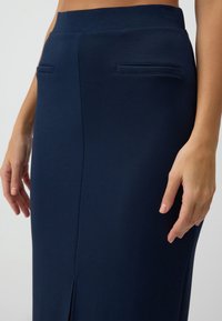 Gonna blu navy realizzata in un tessuto morbido, con vita alta, due tasche cucite e uno spacco frontale per una maggiore libertà di movimento.