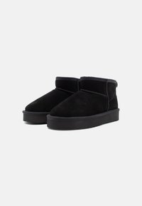 Botas de tobillo de ante negro con puntera redondeada, interior suave y suela de goma. Detalles de costura y un diseño bajo sin cordones.