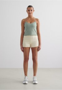 Camisolă ribbed de un verde deschis cu tiv ondulat, asociată cu pantaloni scurți plisati de un crem, având un tiv unduit, purtată cu pantofi sport albi.