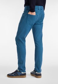 Blaue Baumwollmischung-Hosen mit geradem Bein, hinteren Taschen und einer glatten Textur. Kombiniert mit marineblauen Sneakers.