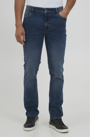 Jeans de mezclilla azul oscuro con corte recto, diseño de cinco bolsillos, costuras visibles y combinados con zapatillas negras de caña baja.