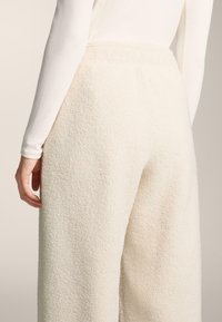 Fehér, plüss lounge nadrág puha, texturált felülettel. A derékrész rugalmas, és a szárak bő szabásúak.