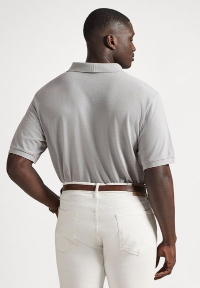 Γκρι κοντομάνικο πόλο πουκάμισο με υφή, προβλημένο από πίσω, σε συνδυασμό με λευκό τζιν και καφέ ζώνη.