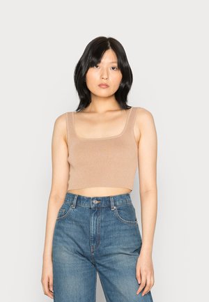 Top cropped beig com nervuras, alças largas, decote quadrado e padrão texturizado, combinado com jeans de denim azul de cintura alta.