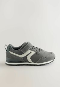 Grauer Sport sneaker mit weißen Seitendetails, Schnürsenkeln und Klettverschluss auf einem neutralen Hintergrund.