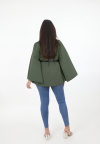 Olivgrön, långärmad topp med vida ärmar, bältad vid midjan. Kombinerad med åtsittande blå jeans och klara klacksandaler.