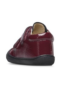 Scarpa in pelle verniciata bordeaux con strap in velcro, suola in gomma nera, forma arrotondata e finitura testurizzata. Progettata per comfort e supporto.