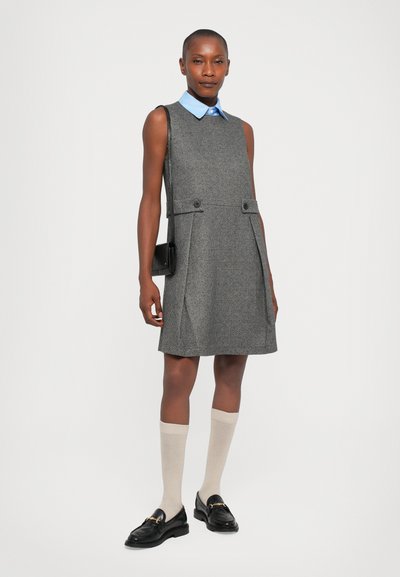 Graues Hahnentrittmuster ärmelloses Kleid mit einem blauen Kragenshirt, zwei Fronttaschen und schwarzen Slippern mit goldenen Akzenten. Texturiertes Material.