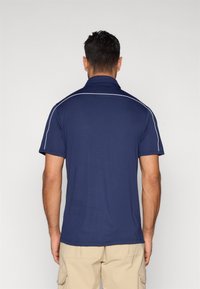 Μπλε ναυτικό πόλο με κοντά μανίκια, γιακά και λευκή επένδυση κατά μήκος των ώμων και του λαιμού. Ομαλό, υφή ύφασμα.