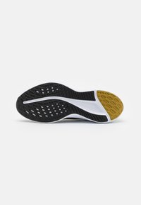 Semelle de chaussure de sport noir et blanc avec motifs de texture pour adhérence ; zone d'accentuation jaune près de l'orteil et rainure centrale pour flexibilité.