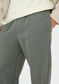 Pantalon de jogging gris avec une texture douce, une taille élastique et deux grandes poches rectangulaires à l'avant.