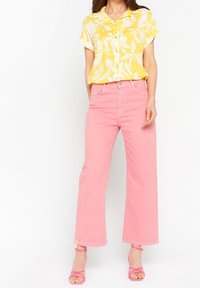 Camisa amarilla de botones con un patrón de hojas blancas, combinada con pantalones anchos rosas. Atuendo complementado con sandalias rosas de tiras.