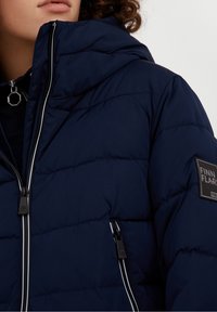 Námořnická puffer bunda s vysokým límcem, s předním zipem, bílými akcentními stehy a čtvercovou logem na levém rameni.