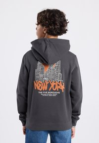 Felpa con cappuccio grigio scuro e una grande grafica arancione di grattacieli di New York con testo sul retro. Tessuto morbido con una vestibilità standard e cappuccio.