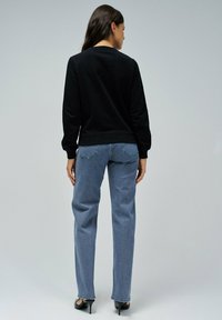 Sudadera negra de cuello redondo, combinada con jeans rectos de color azul claro. La modelo lleva tacones negros, mostrando un diseño minimalista.