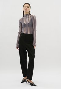 Langdurige mouwen, gestreept top van doorschijnende stof met een hogere halslijn, gecombineerd met zwarte op maat gemaakte broeken en puntige zwarte hakken.