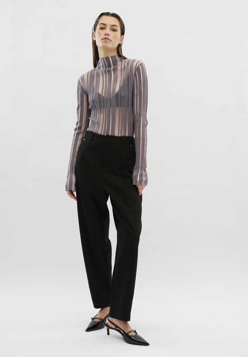 Langdurige mouwen, gestreept top van doorschijnende stof met een hogere halslijn, gecombineerd met zwarte op maat gemaakte broeken en puntige zwarte hakken.