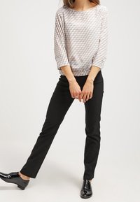 Blouse rose clair avec un motif texturé en forme de bulles, col arrondi et manches trois-quarts. Associée à un pantalon noir ajusté et des chaussures noires brillantes.