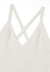 Bralette bianco lavorato a maglia con design a V, caratterizzato da spalline incrociate e un motivo testurizzato di strisce e piccoli fori.