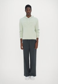 Felpa verde chiaro con logo in rilievo, abbinata a pantaloni grigi scuri a vestibilità larga e sneakers bianche. Design semplice e minimale.
