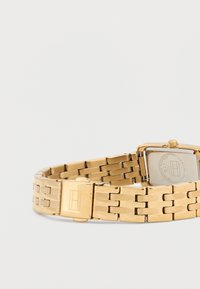 Gold wristwatch with a rectangular case and metal link strap. The watch features a silver dial and a clasp with a logo detail.