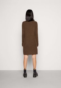 Brun stickad klänning med långa ärmar, rund halsringning och A-linjeform, kombinerad med svarta ankelstövlar med en gul hälflik.