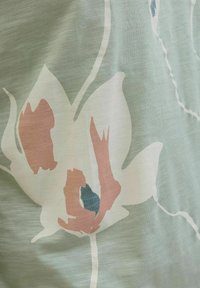 Gėlių audinys su didelėmis baltomis gėlėmis, dekoruotomis rožinėmis ir mėlynomis akcentais, švelniame žaliame fone. Lengvas, tekstūruotas medžiaga.