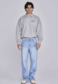 Light gray pullover with a quarter zipper and logo detail, paired with light blue denim jeans, and cream-colored sneakers.