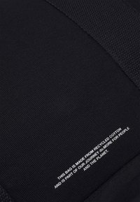 Sac noir fabriqué en coton recyclé. Présente un tissu texturé avec une section lisse et un texte imprimé blanc en détail. Design simple, usage pratique.