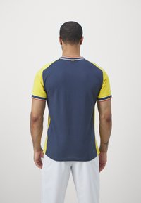 Polo tričko s krátkým rukávem v námořnické modré barvě, žlutými raglánovými rukávy a barevným pruhovaným límečkem. Vyrobeno z texturovaného materiálu.