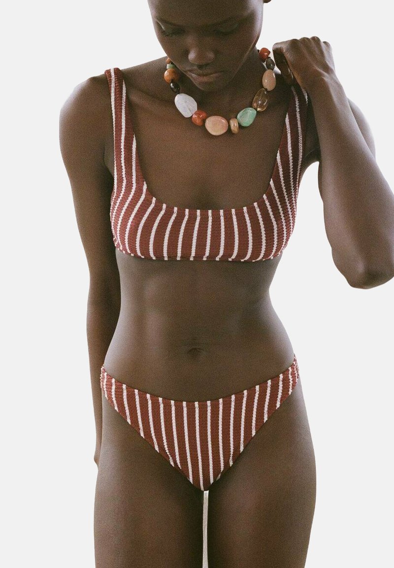 Set bikini a righe ruggine e crema, realizzato in tessuto testurizzato. Presenta un top con scollatura quadrata e un fondo a vita bassa, completato da una collana con perline spesse.