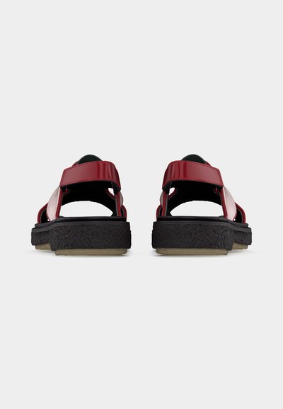 Κόκκινα σανδάλια με μαύρες υφασμάτινες σόλες και ρυθμιζόμενα λουράκια, από πίσω, σε ανοιχτό γκρι φόντο.