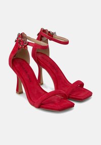 Rote Wildleder-Pumps mit hohen Absätzen, quadratischer Spitze, Knöchelriemen und dekorativen Juwelenakzenten, ausgestattet mit einer gepolsterten Innensohle und schmalem Absatz.